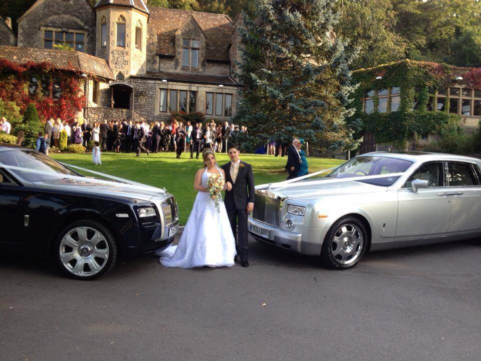 Wedding guests, bride and groom having photoshoot on grass next to two vintage classical cars